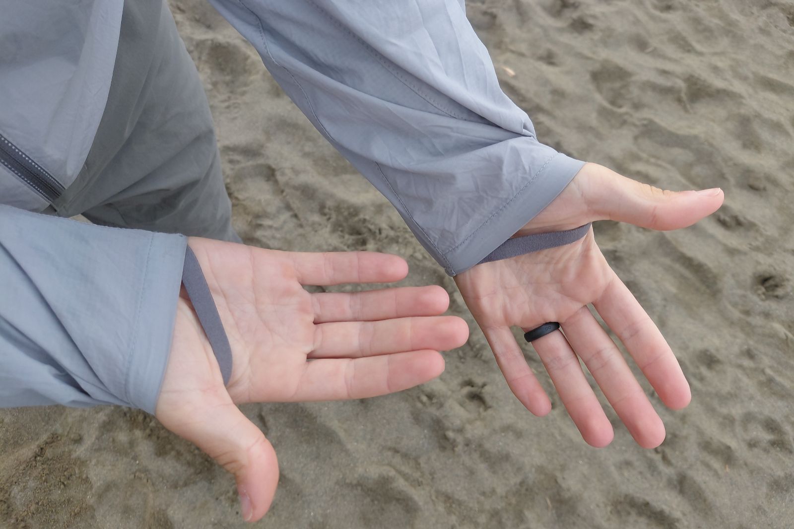 Two hands in gray, lightweight jackets with thumb loops are open against a sandy background.