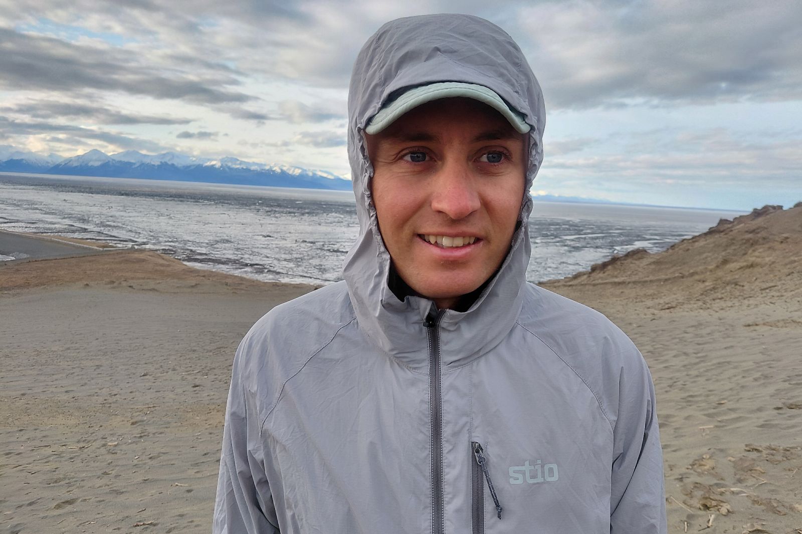 A man wears a gray windbreaker with the hood up.