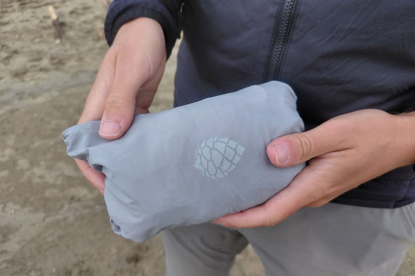 A man holds a windbreaker bundled into a small packable ball.