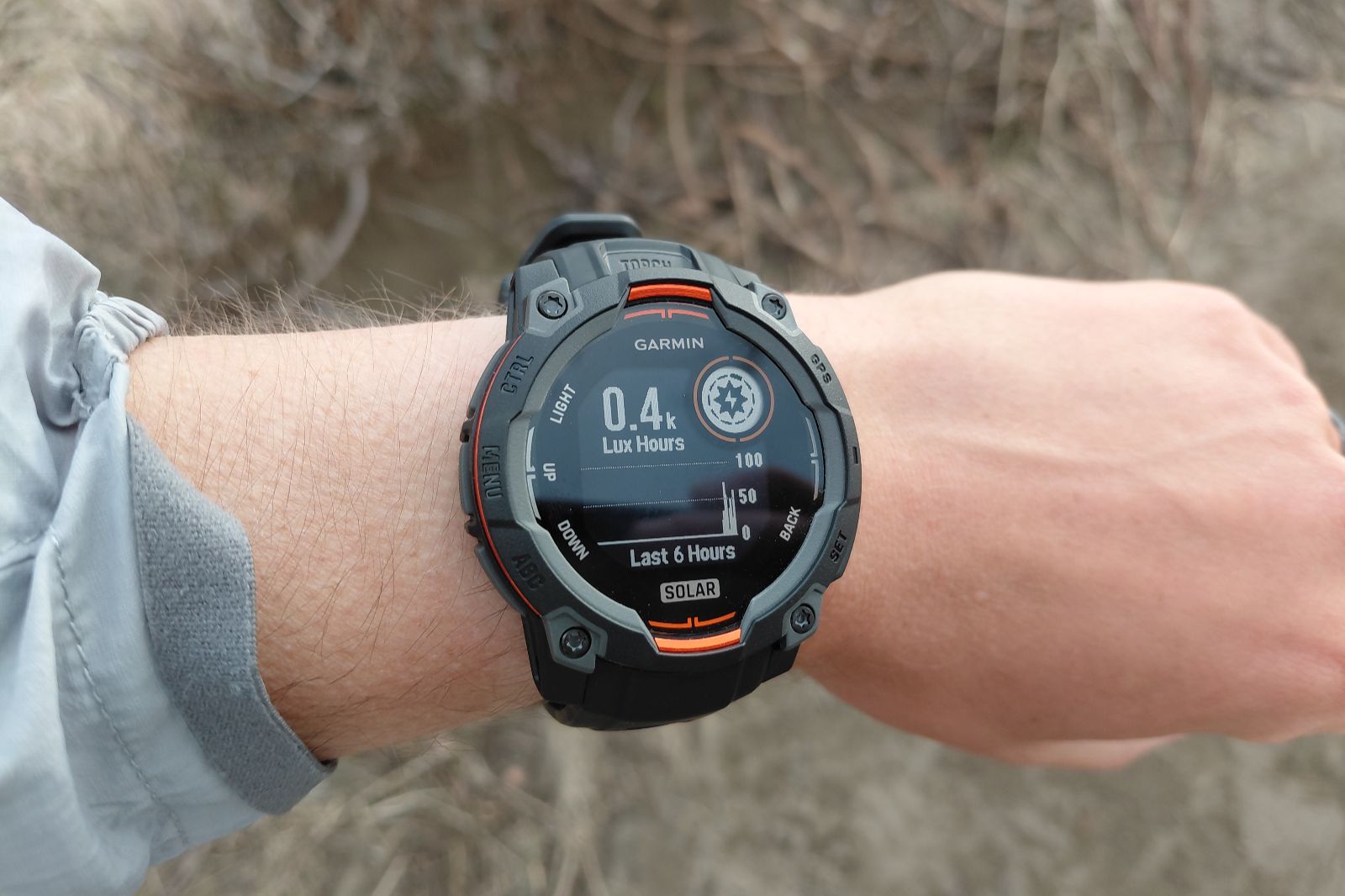 A close-up of a person's wrist wearing a black and orange Garmin solar smartwatch displaying solar intensity.