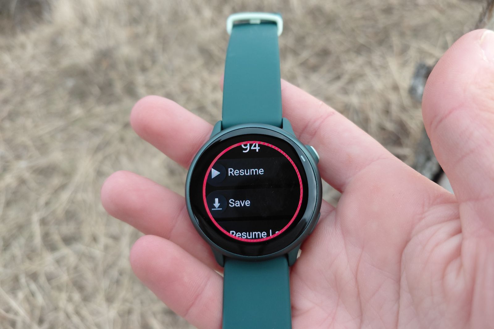 Close-up of a hand holding a smartwatch with a green strap, displaying options to "Resume" or "Save" on screen.