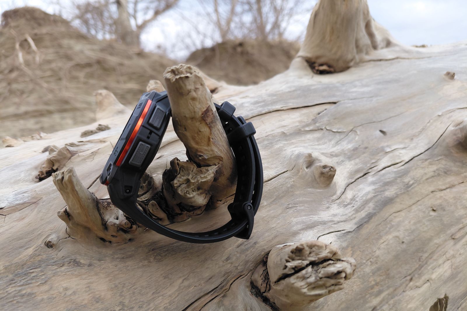 Smartwatch with black strap and orange accents resting on a weathered driftwood log.