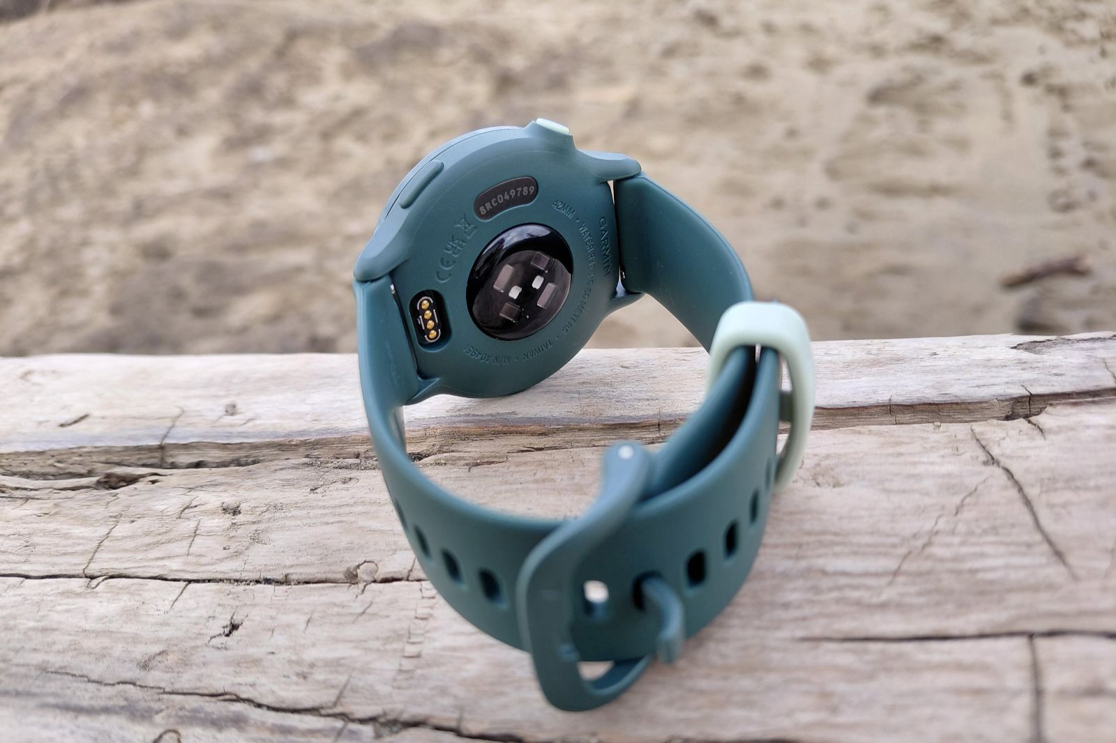 A teal smartwatch lies face down on a weathered wooden surface, showing its sensor and wrist strap.