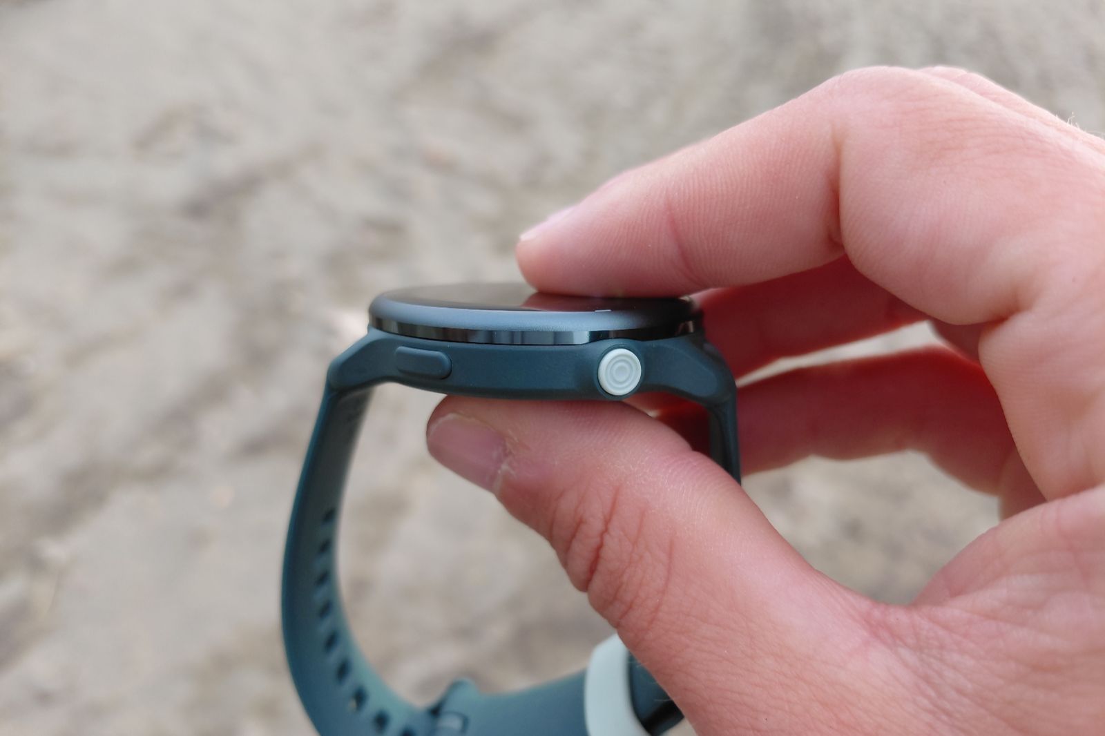 A hand holds a smartwatch showing its side buttons and low profile.