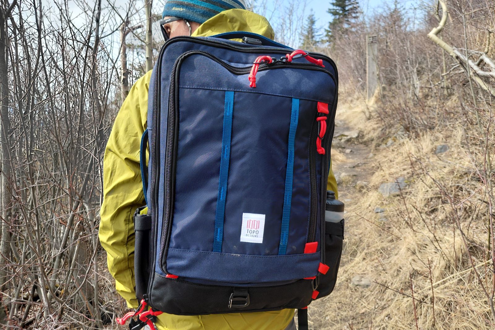A person wearing a blue backpack with red accents on a hiking trail.