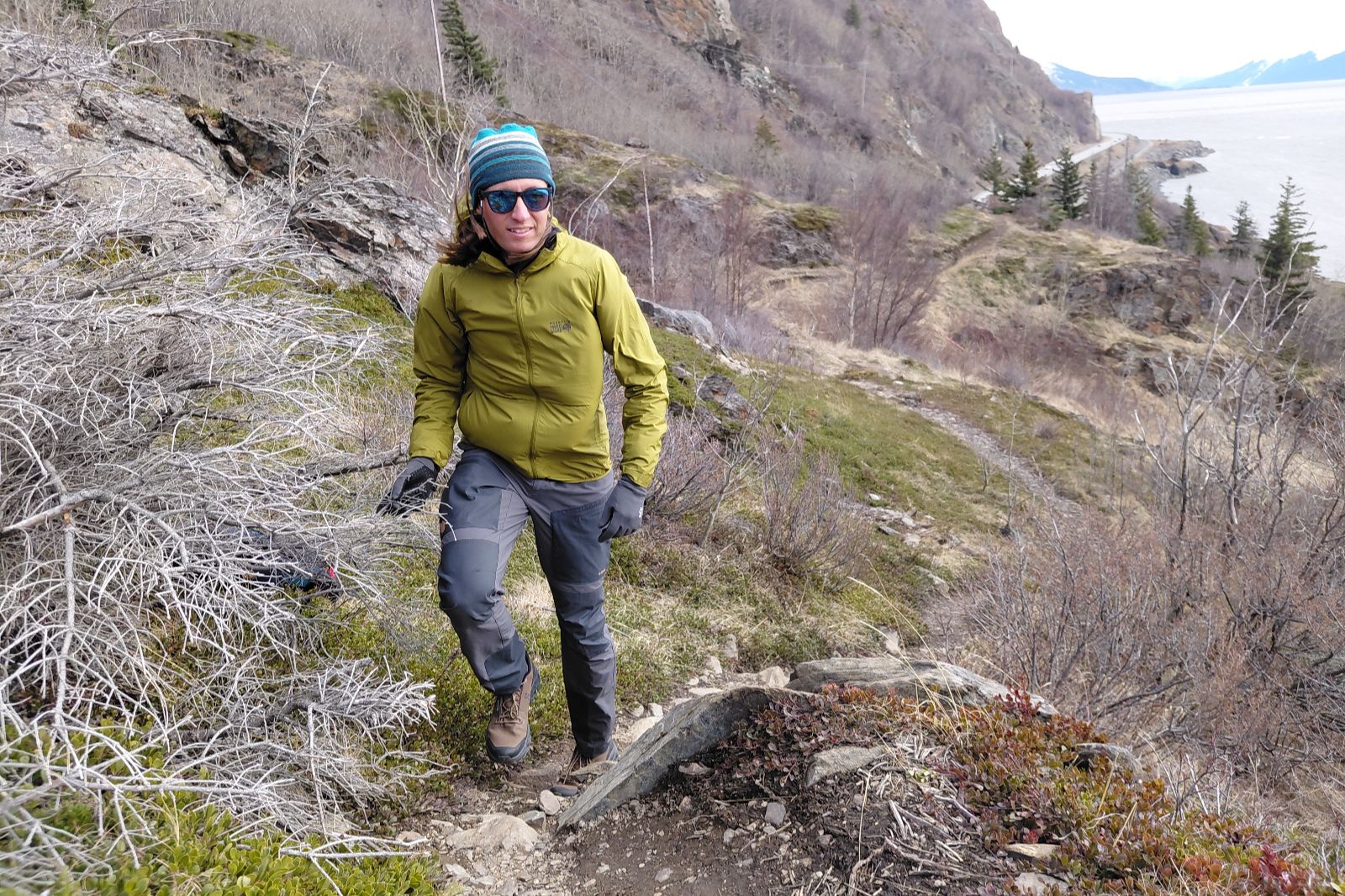 A person hikes uphill on a rocky trail wearing a green jacket.
