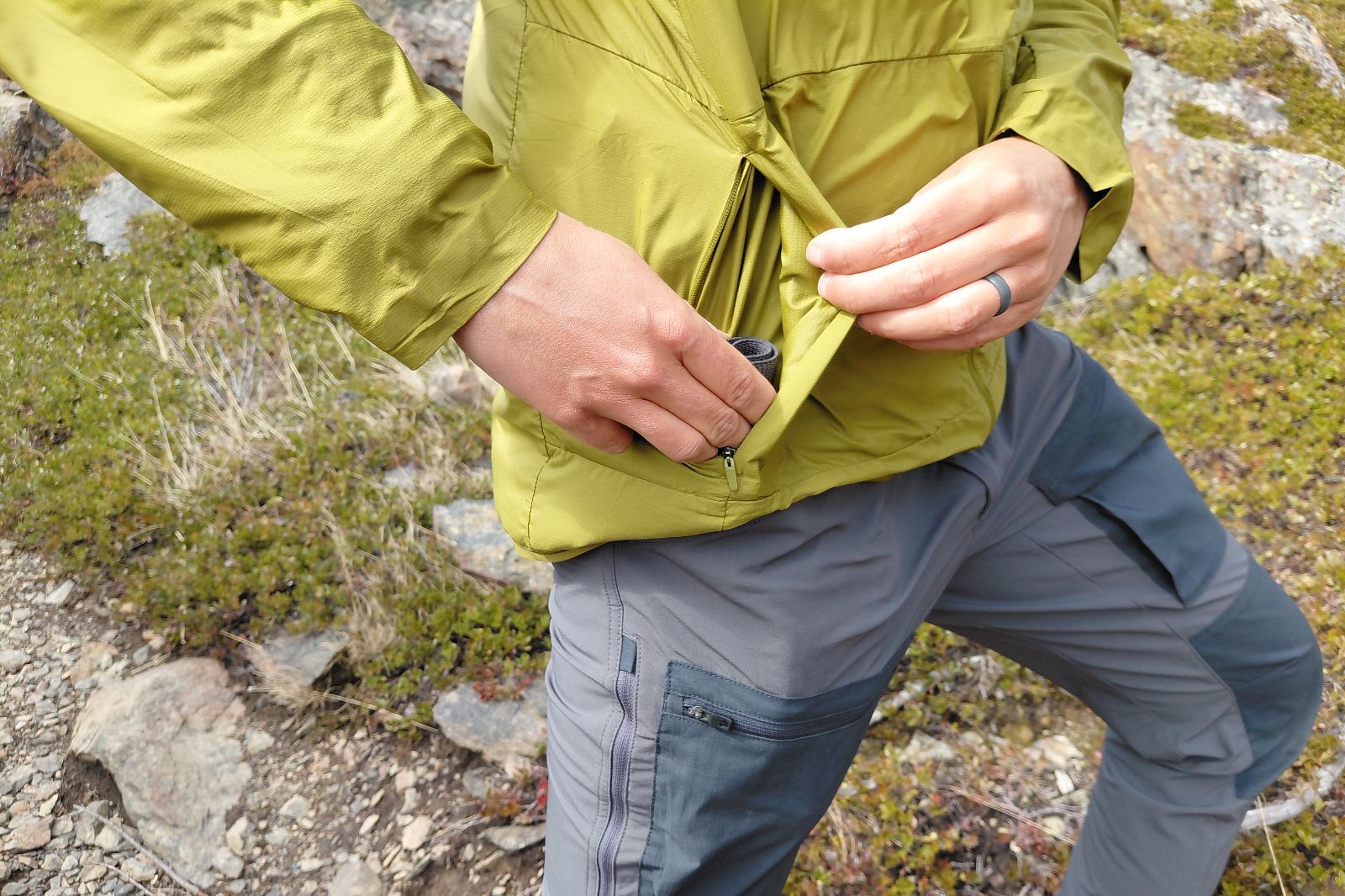 A person puts an item in the pocket of their green jacket.