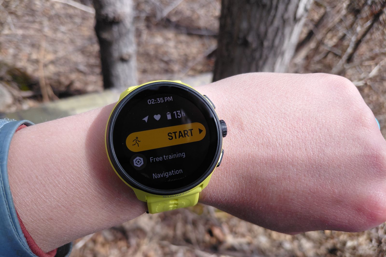 A person wearing a yellow smartwatch displaying a fitness app with a start button.