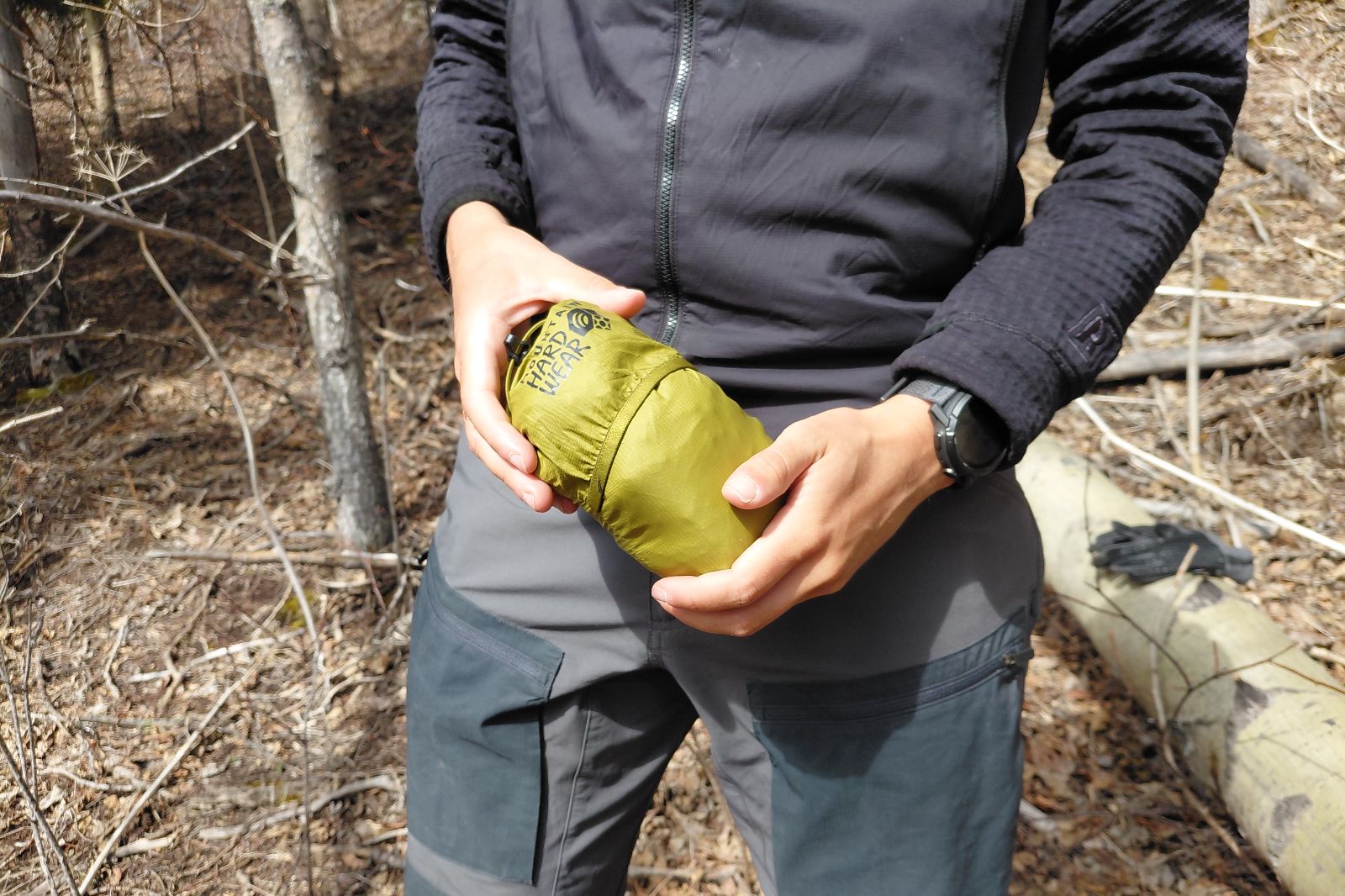 A person in outdoor attire holds a small, compact green windbreaker.
