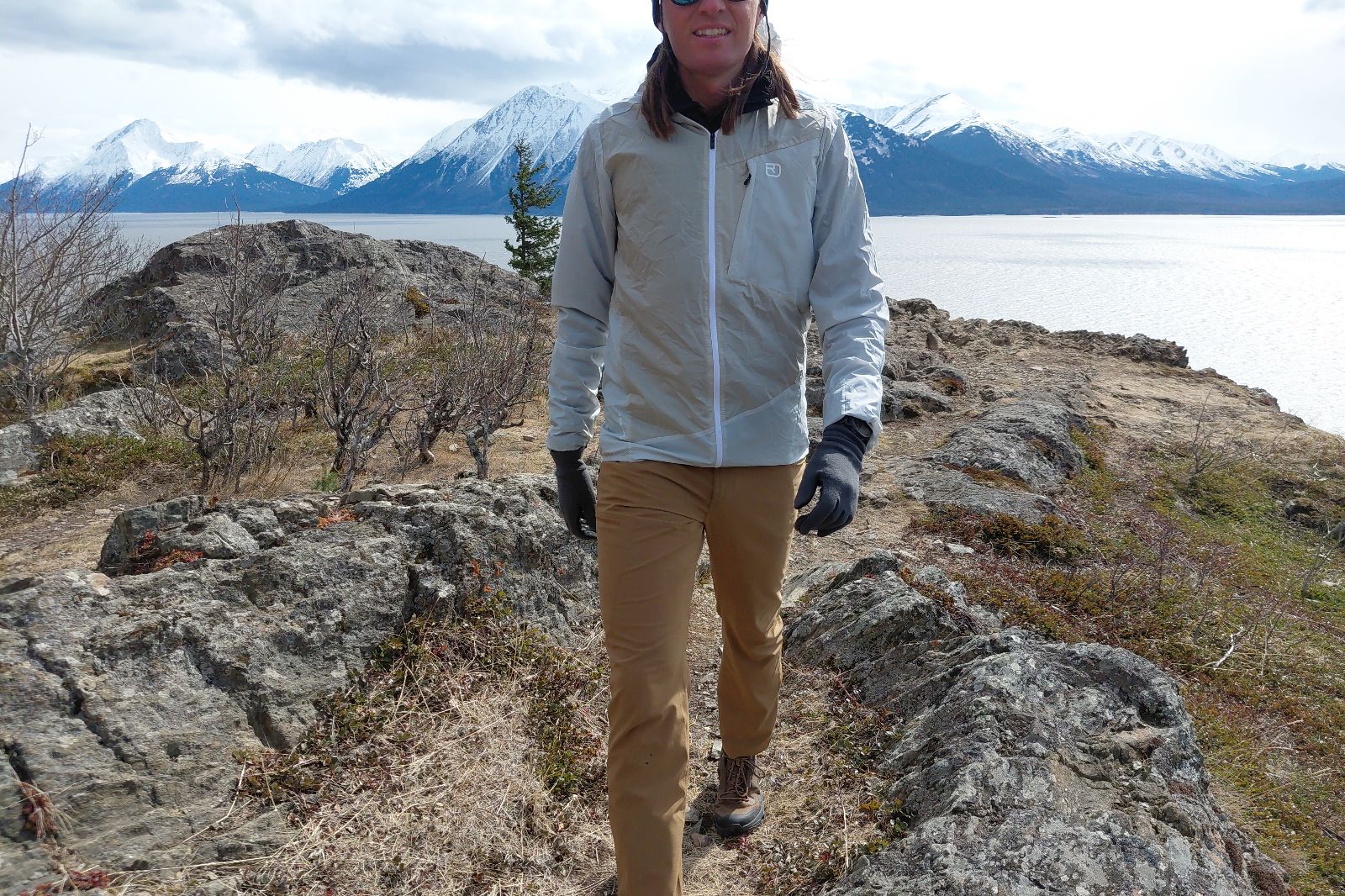A person wearing a light jacket and brown pants hikes on a rocky trail above the ocean.