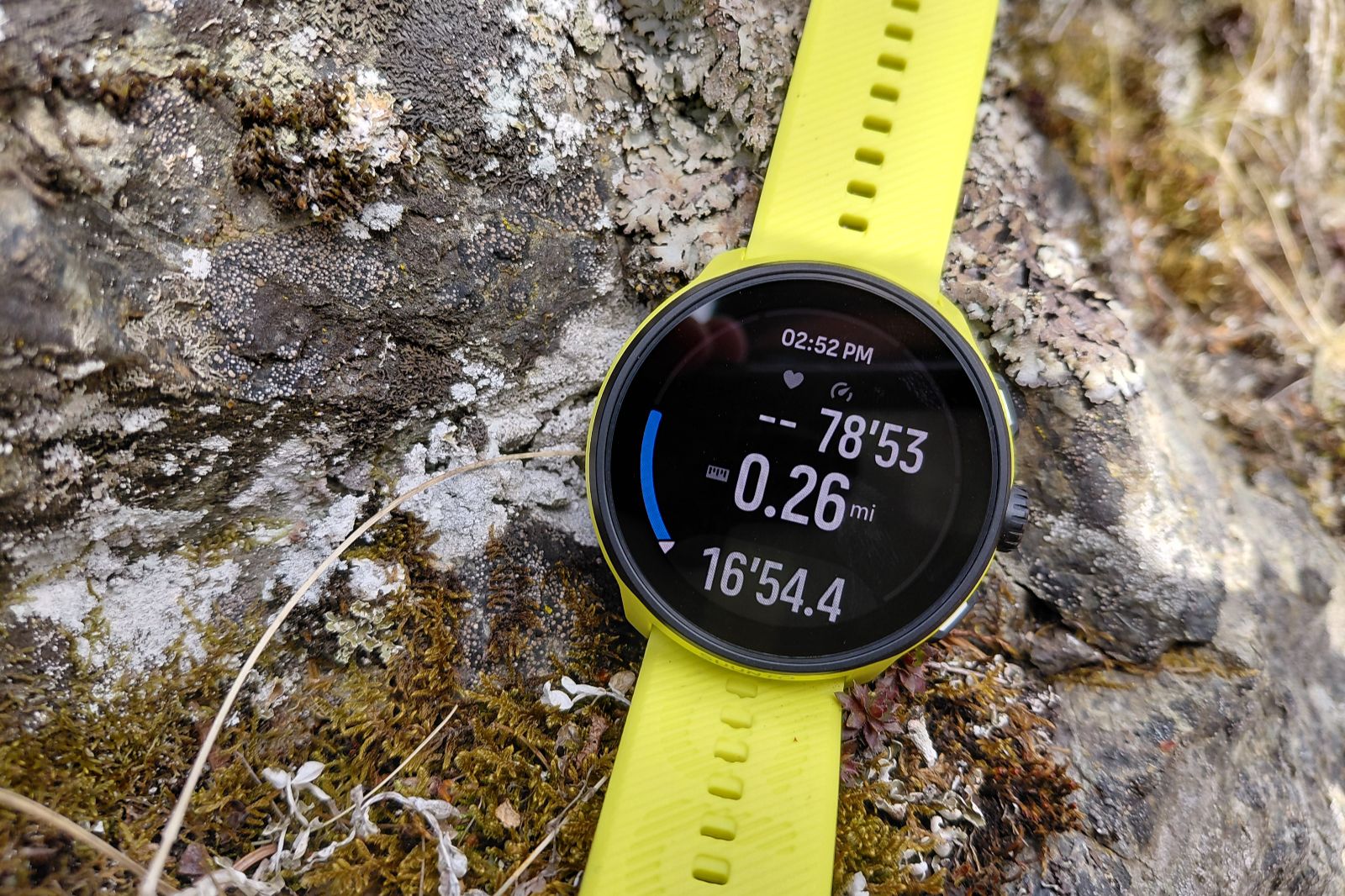 A yellow watch rests on a mossy rock, showing running stats.