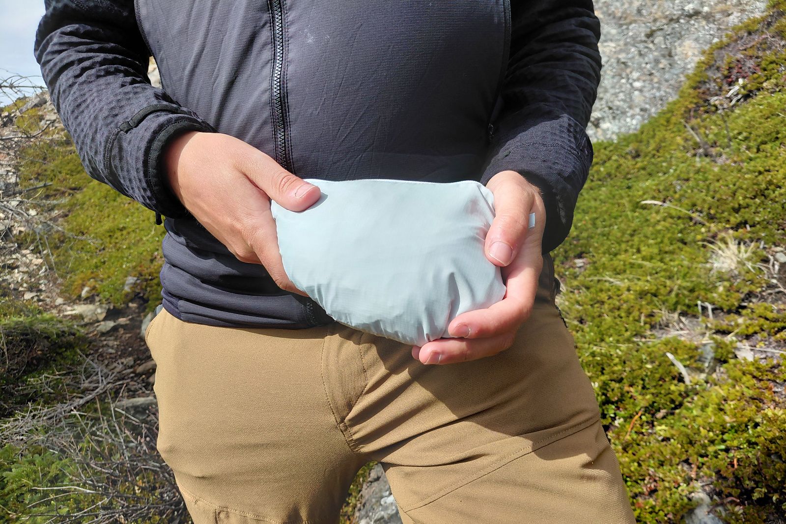 A man holds a jacket stowed in a bundle.