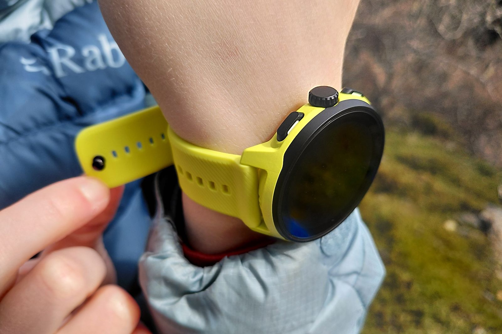Person adjusting a bright yellow sports watch on their wrist outdoors.