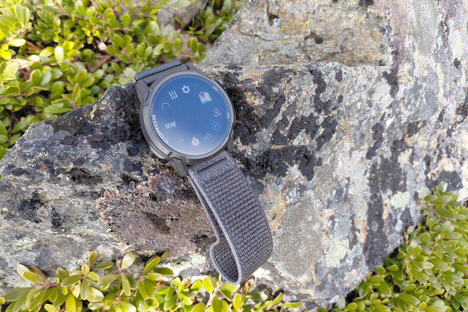 Smartwatch with a gray strap resting on a rugged rock, displaying map and icons.