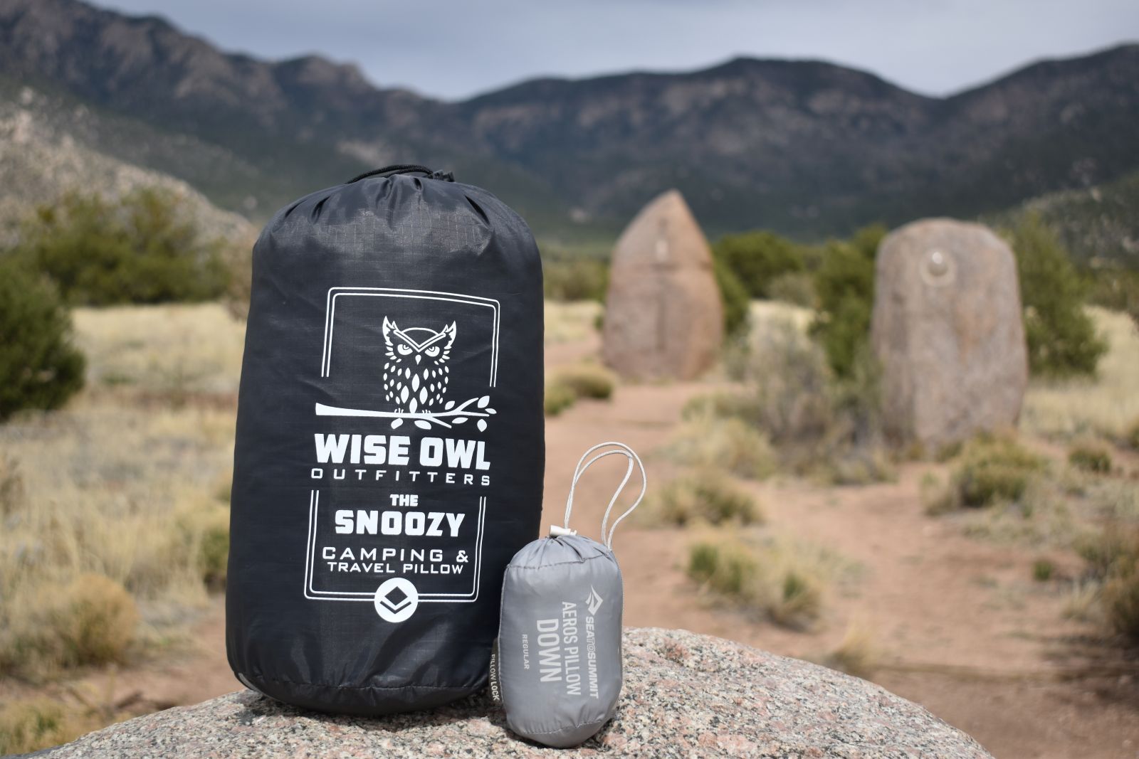 A large camping pillow and small backpacking pillow sit next to each other on a rock to demonstrate differences in their packed size