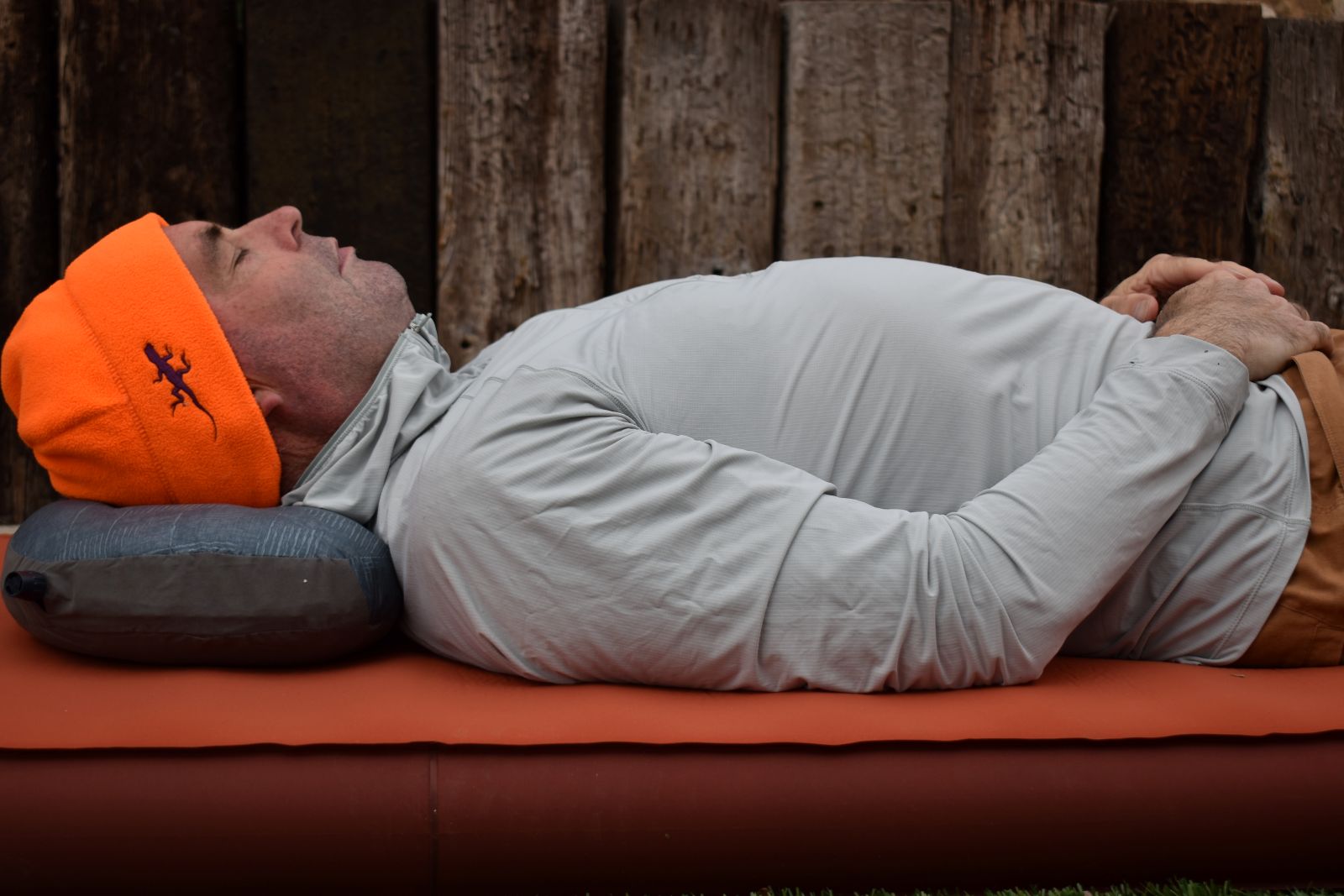 A hiker lays on a camping mattress with the Air Head Down Pillow under his head.