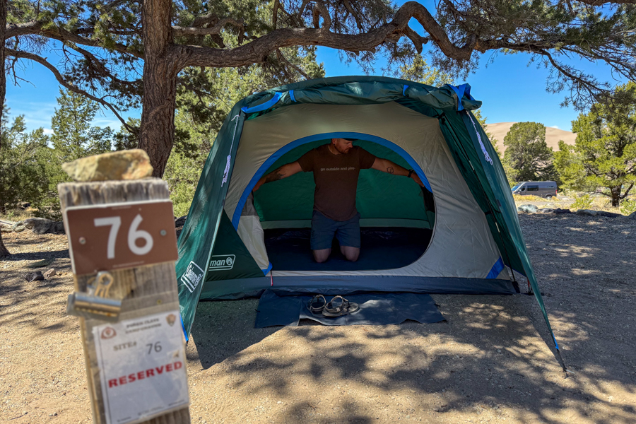 The Coleman Skydome 4 tent pitched with the front vestibule deployed, with a man kneeling inside to show the doorway size and interior space.