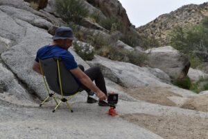 A backpacker reaches for his Jetboil stove while sitting in the Helinox Chair Zero LT.