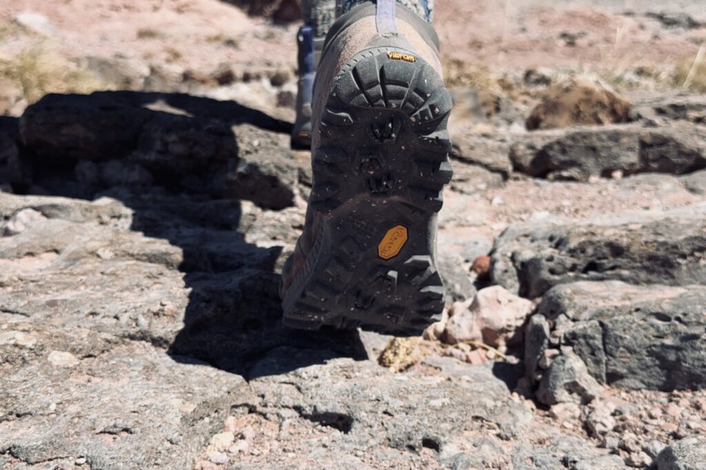 Closeup of the tread on a TX hike boot as a person walks away from the camera on some rocks.