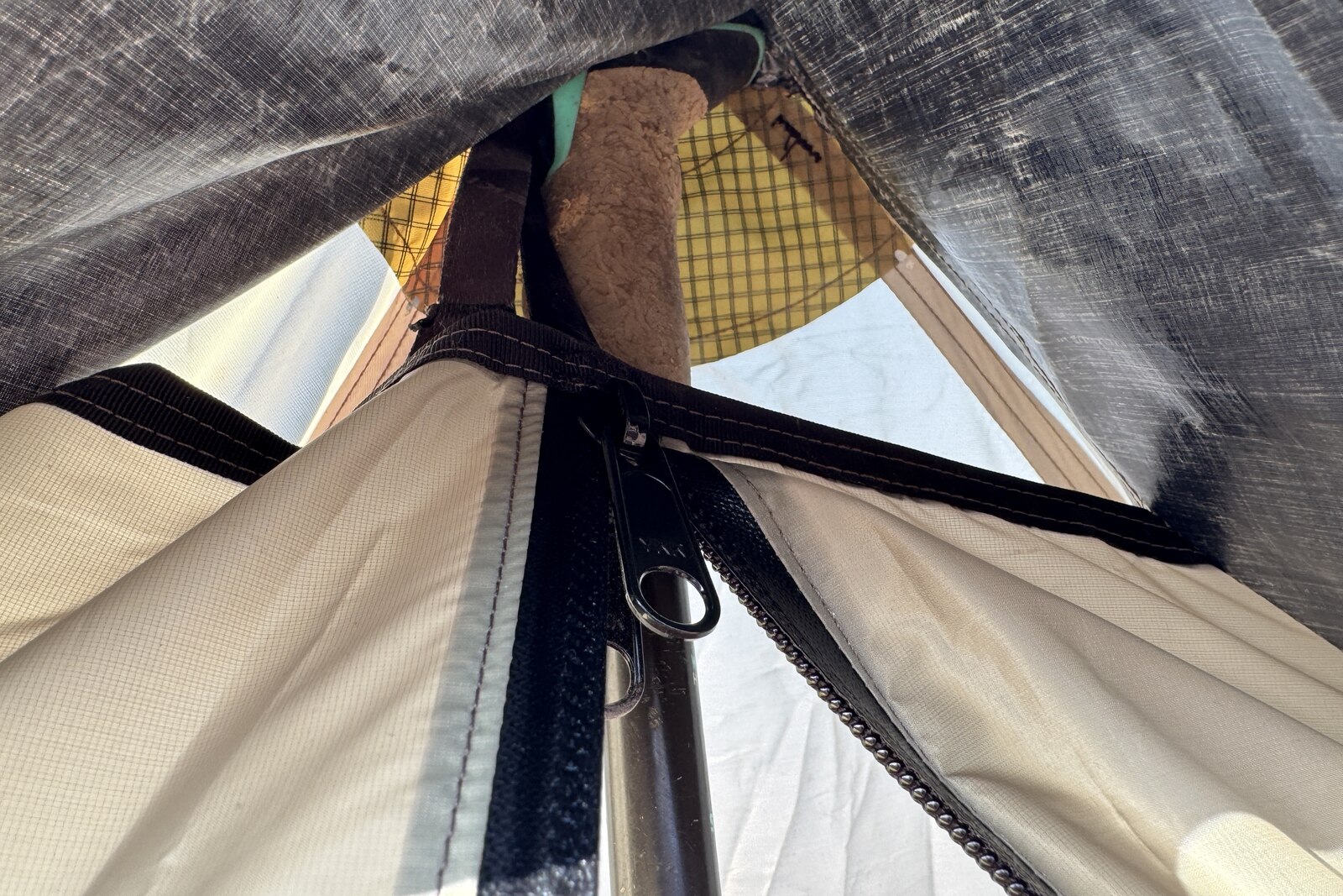 A close up of the vent hole on the MLD tent with the front zipper visible and trekking pole behind it that is holding up the tent.