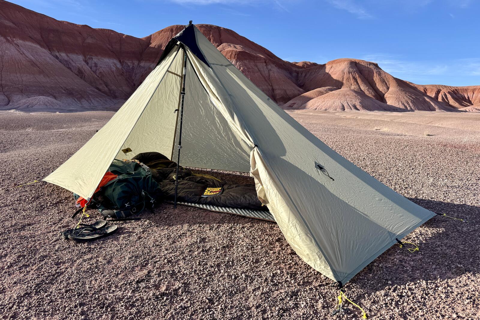 The MLD tent is setup in the badlands with a backpack, sleeping pad, and sleeping bag inside. Only on door is open.