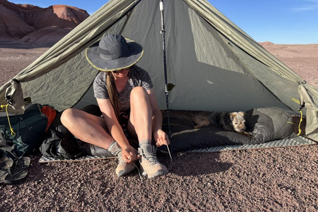 A person is tying the laces of the TX Hike boots while sitting inside a tent. They are in the badlands of Petrified Forest National Park.