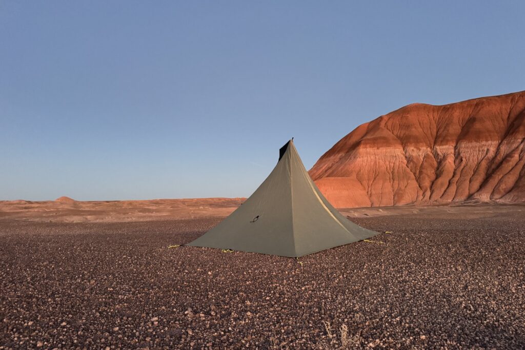 The MLD tent is setup on open ground with badland formations in the background. The sky is clear and there is a reddish hue to the formations.