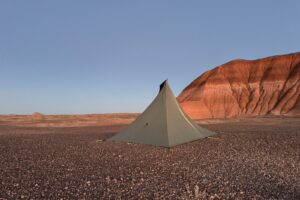 The MLD tent is setup on open ground with badland formations in the background. The sky is clear and there is a reddish hue to the formations.
