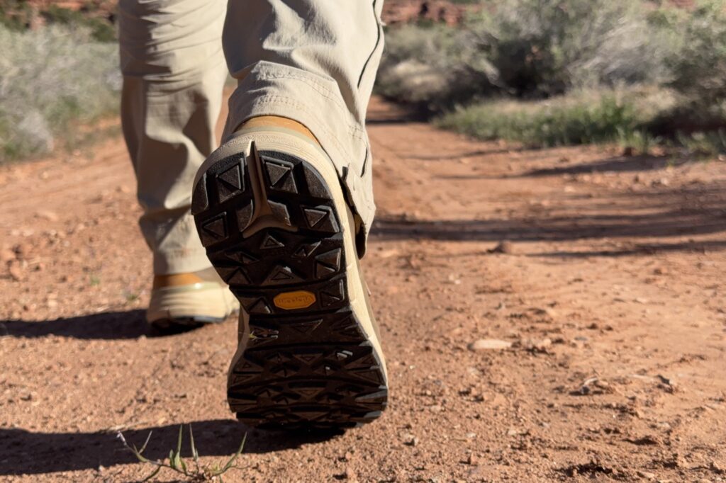 A closeup of the traction on the Danner boots as a person wearing them walks away from the camera on a red dirt road.