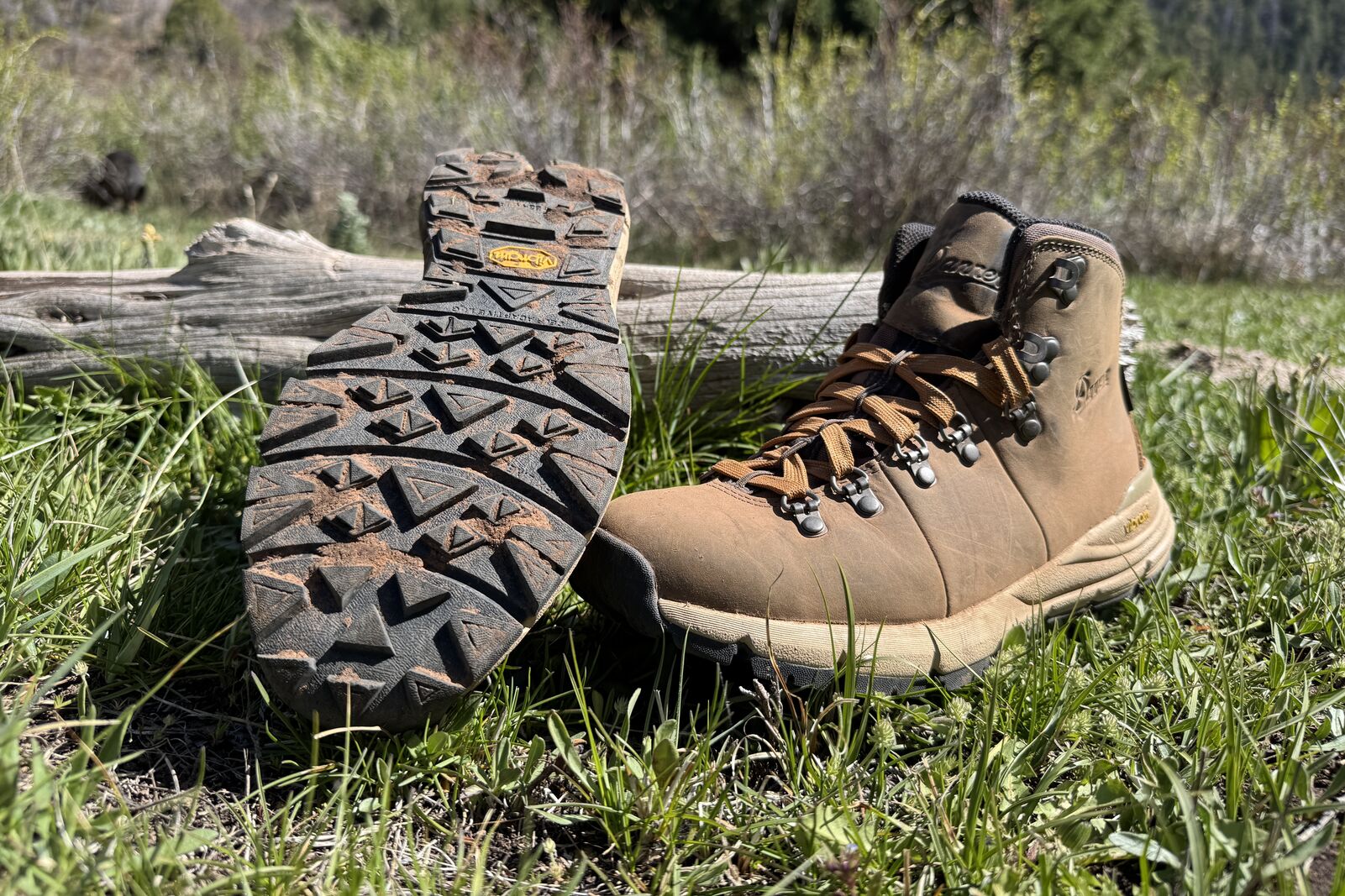 A close up of the Danner boots sitting in some grass. One is turned over to show the tread.