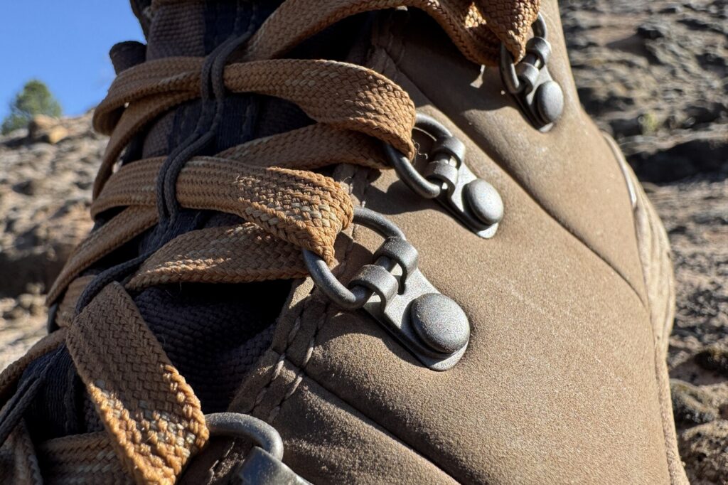 A closeup of the metal eyelets on the Danner boots. There is a rocky slope in the background and it is a clear afternoon.