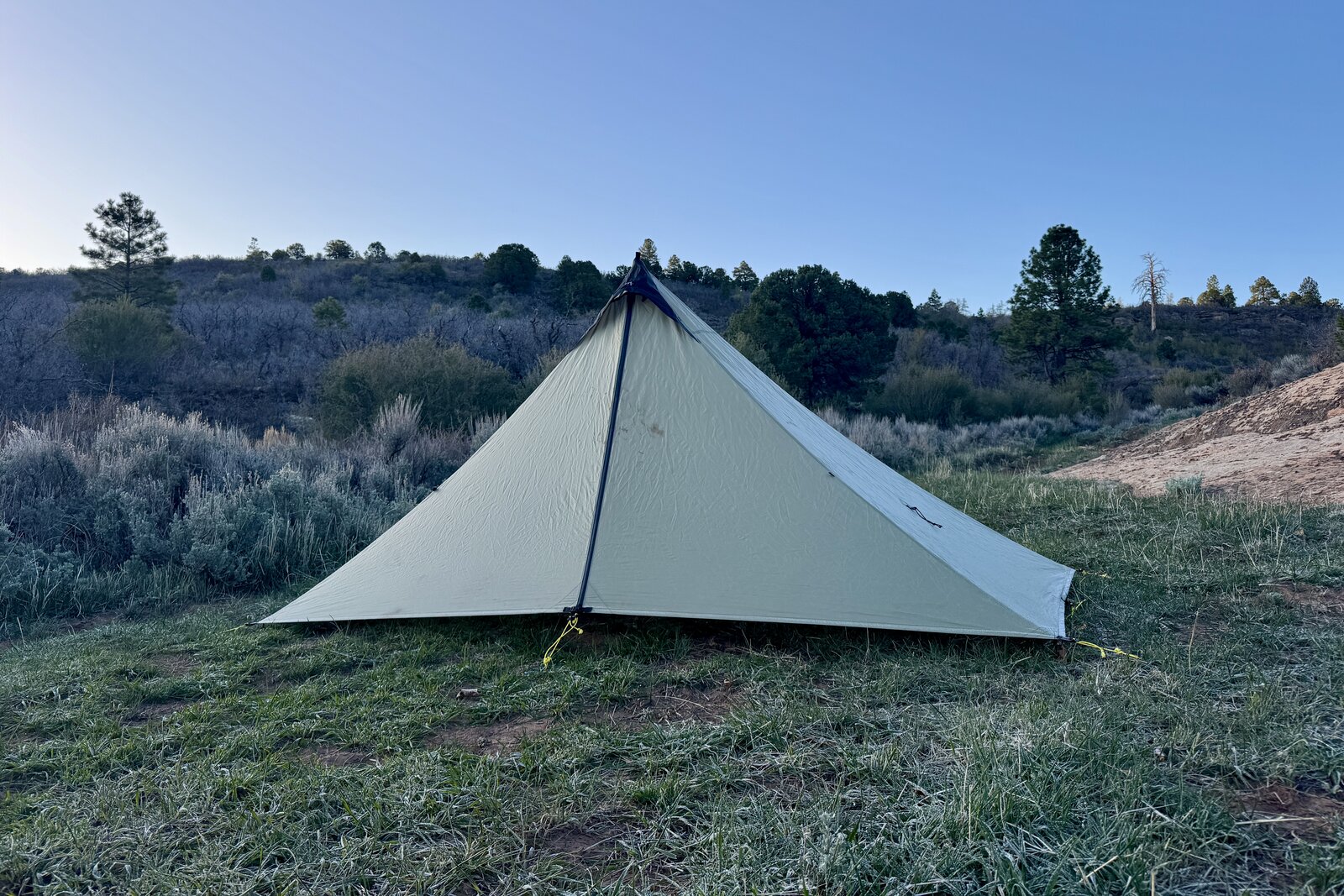 The MLD Tent is setup in a grassy area on a clear morning with sage brush, pinions, and some Ponderosa trees in the background.