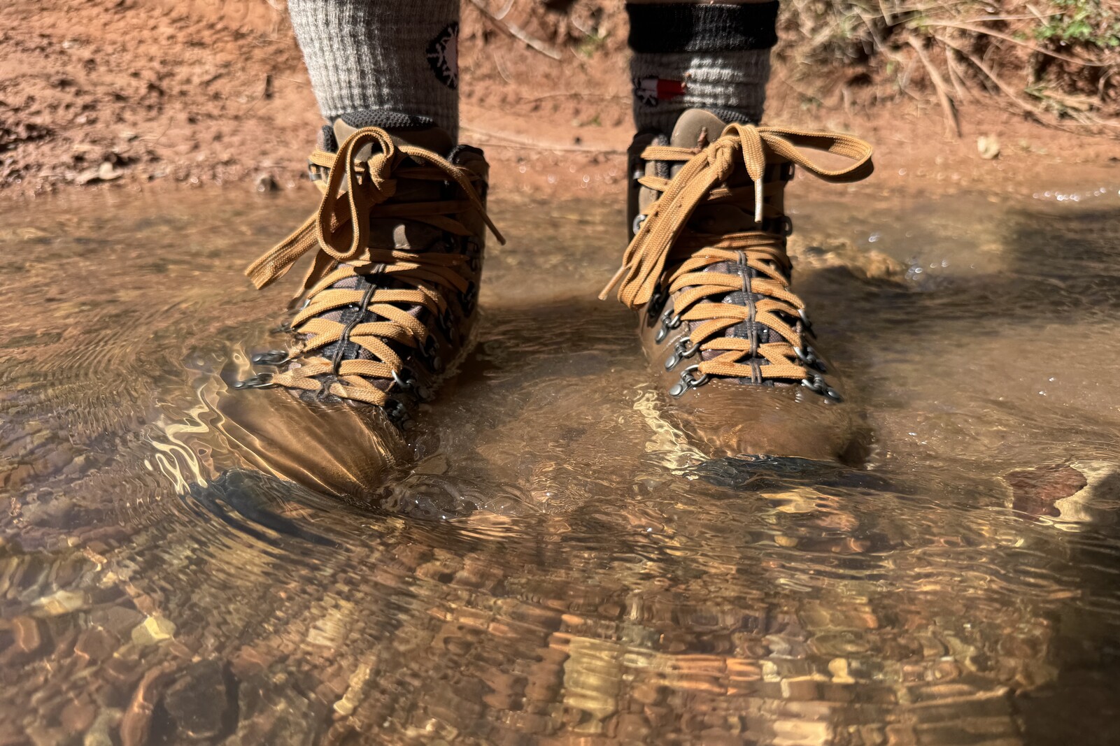 A closeup of the Danner boots as a person stands in the middle of a small stream.