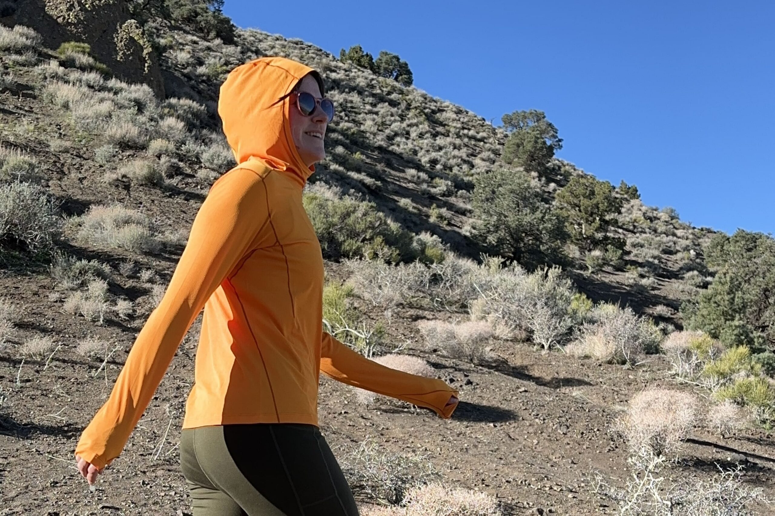 A woman in a bright orange shirt hiking through the high desert.