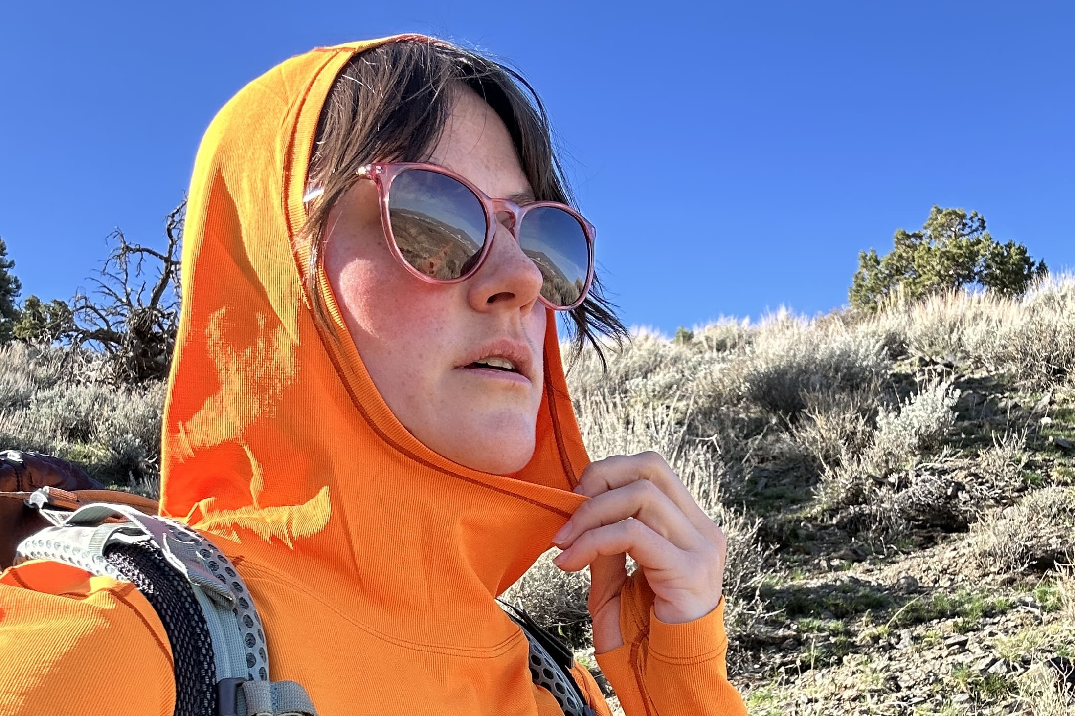 A woman in a bright orange shirt looking into the distance.