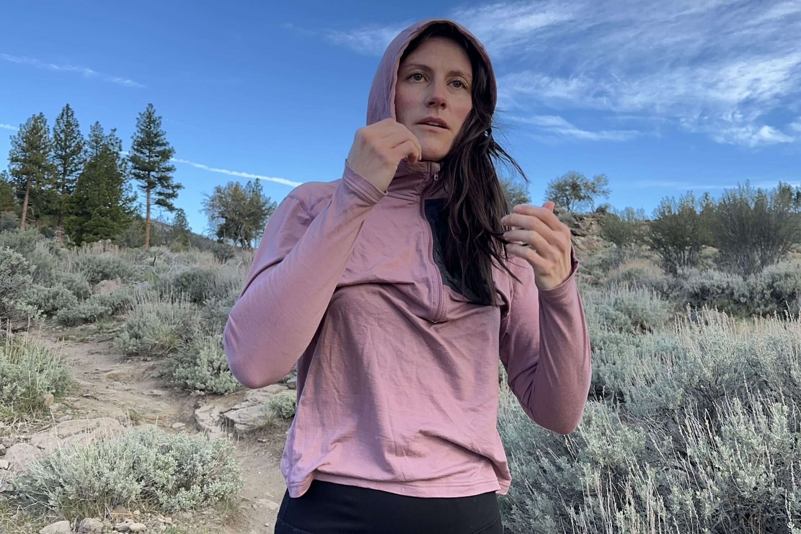 A woman in a pink shirt hiking with sage in background.