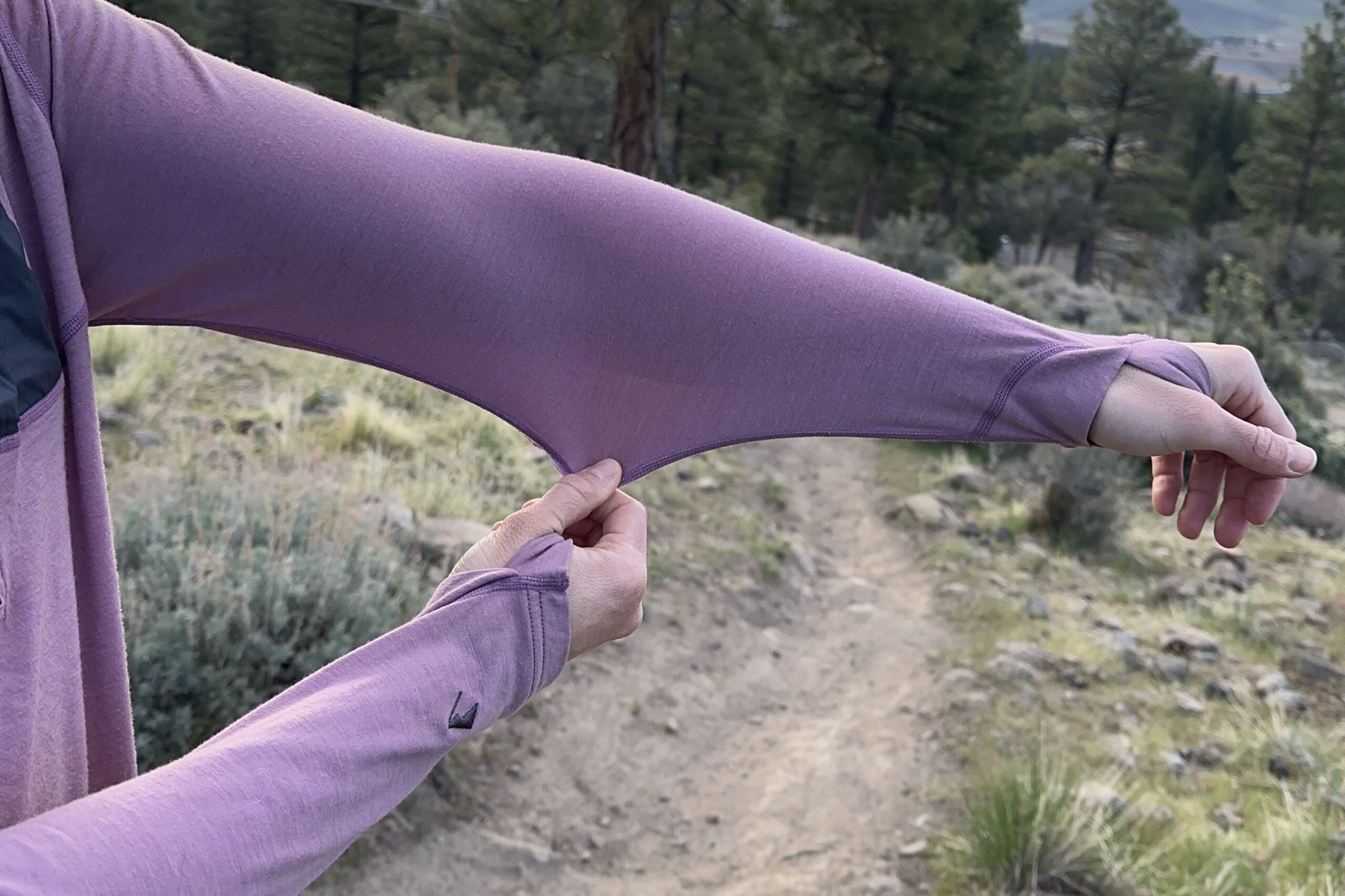 A woman holds out her arm and pulls down the fabric of her shirt to show how stretchy the fabric is.