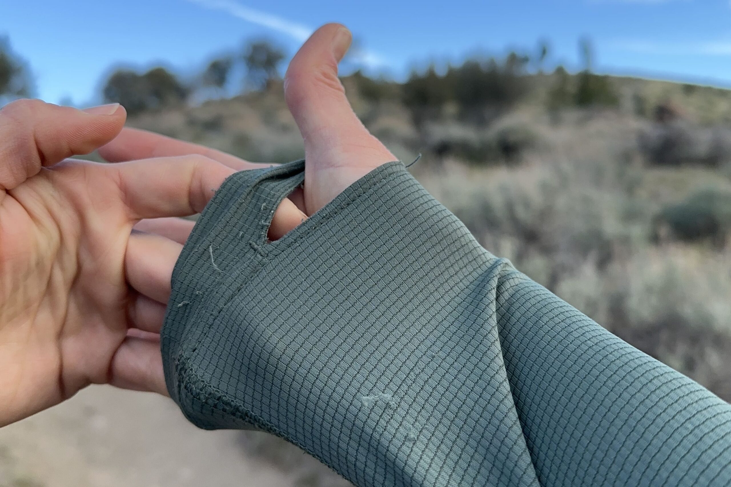 A woman holds out the cuff of her shirt to show the snags in the fabric.