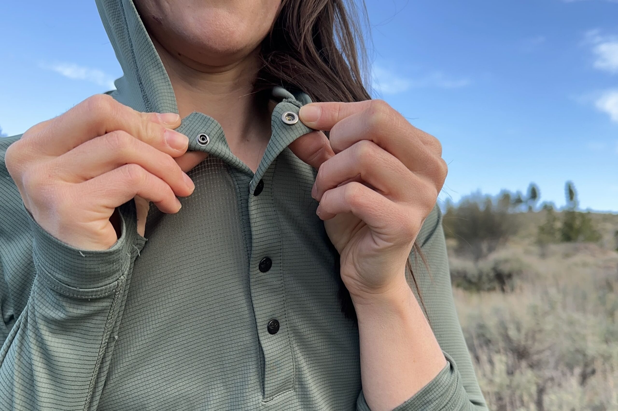 A woman snaps the top button of her sun shirt.