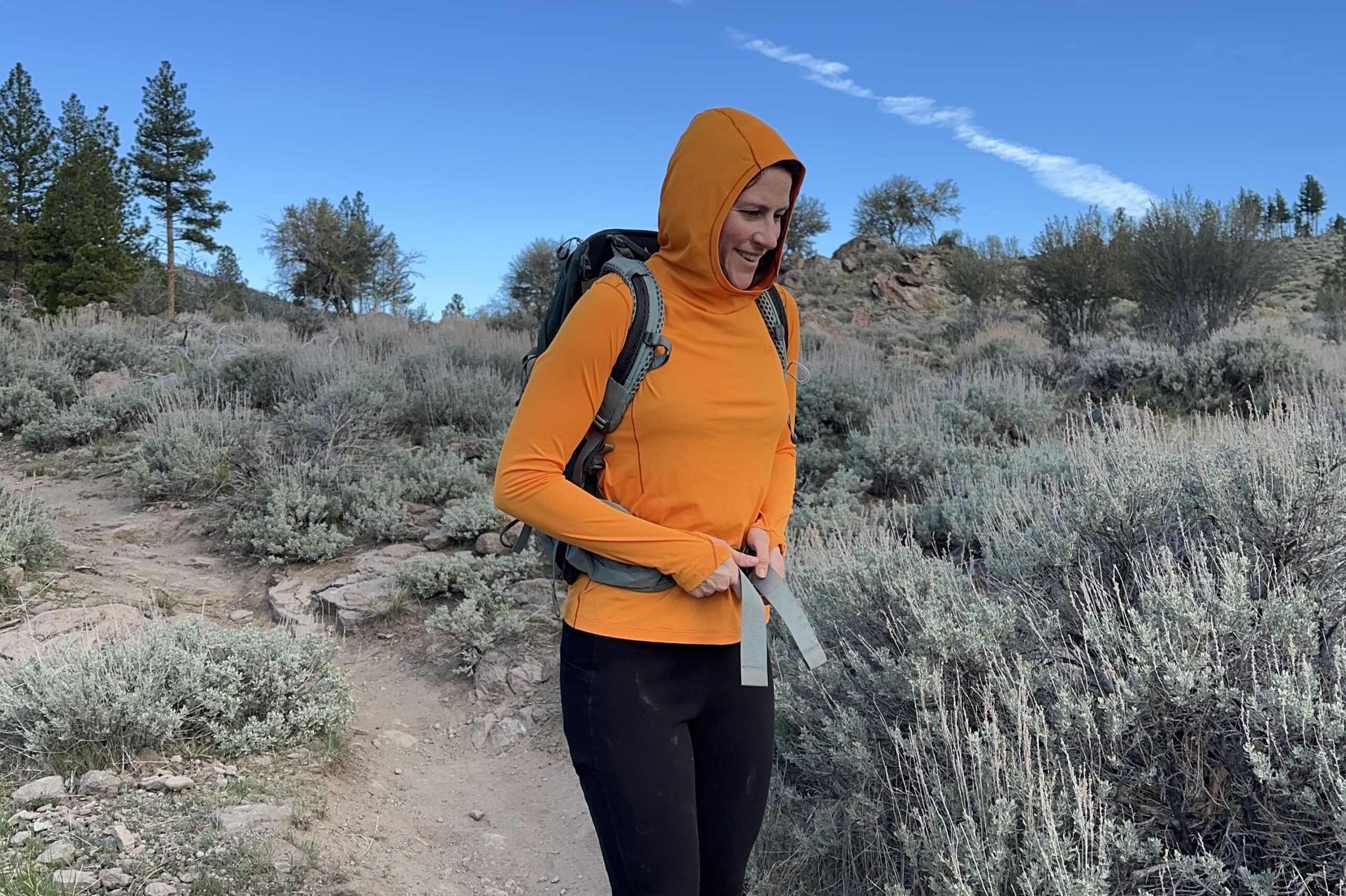 A woman cinches on a day pack while hiking.