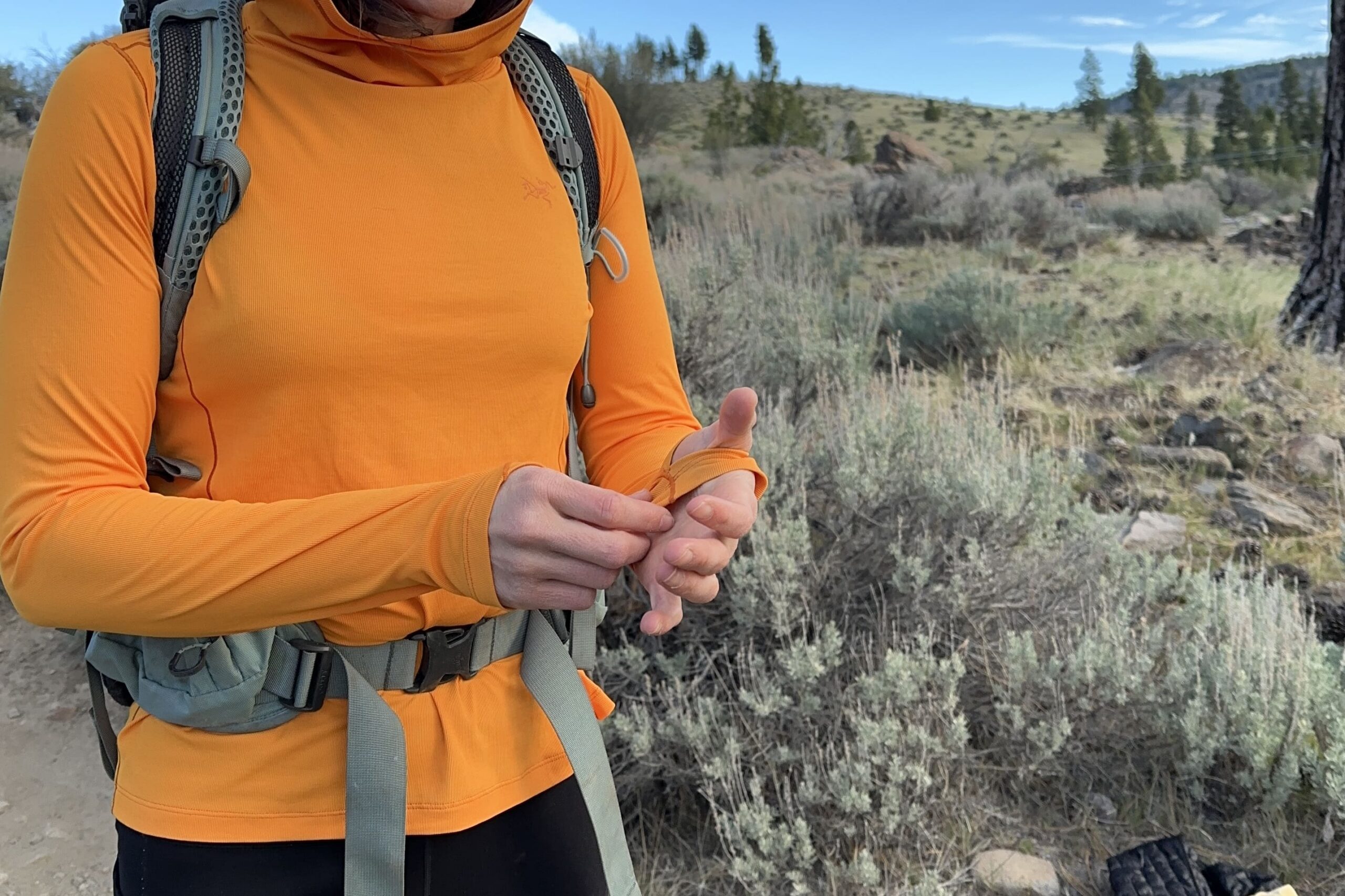 A woman in orange pulls on the sleeve of her shirt.