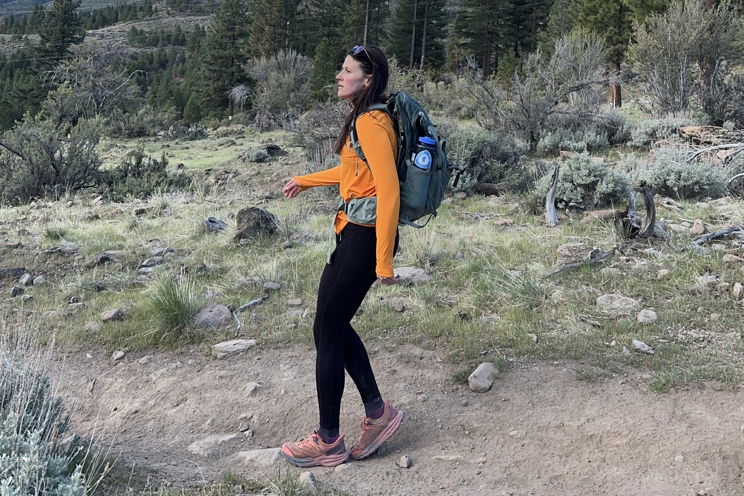 A woman in a bright orange sun shirt hikes in the high desert.