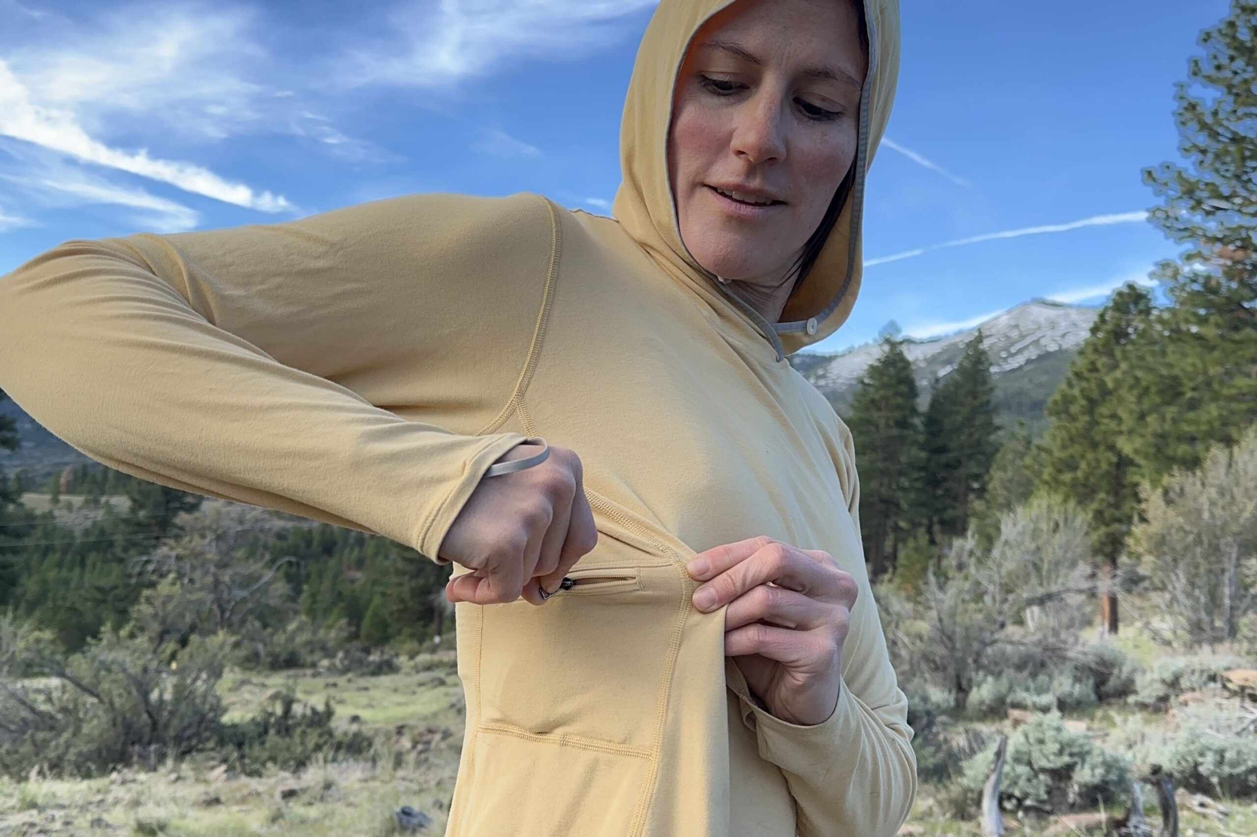 A woman unzips a pocket on the side panel of her shirt.