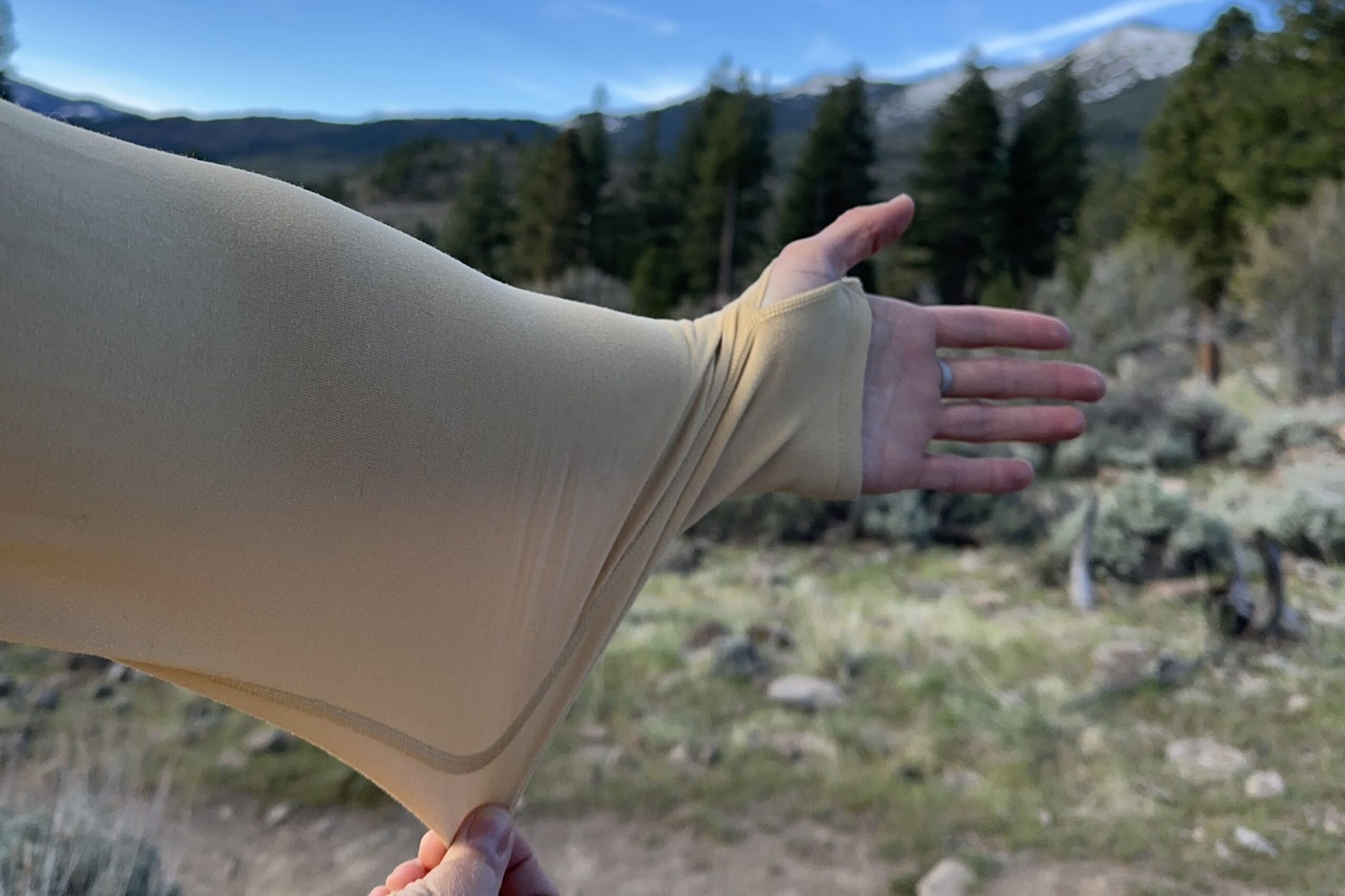 A woman holds out her arm and pulls down the fabric to showcase how stretchy the fabric is.