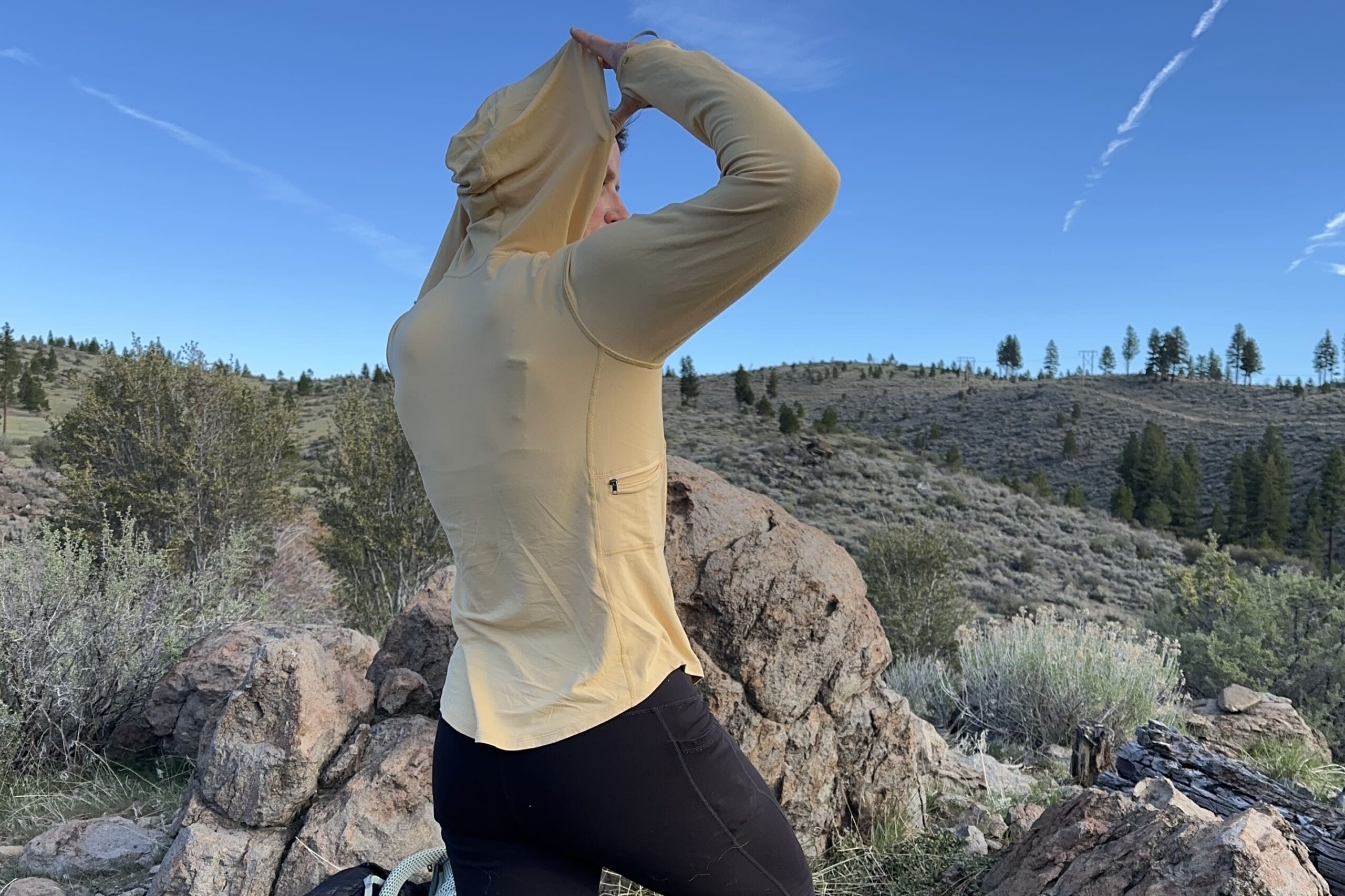 A woman in a yellow sun shirt adjusts the hood of the shirt.