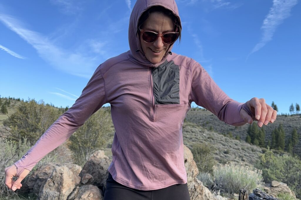 A woman in a pink sun hoodie walks across rocks in a high desert landscape.