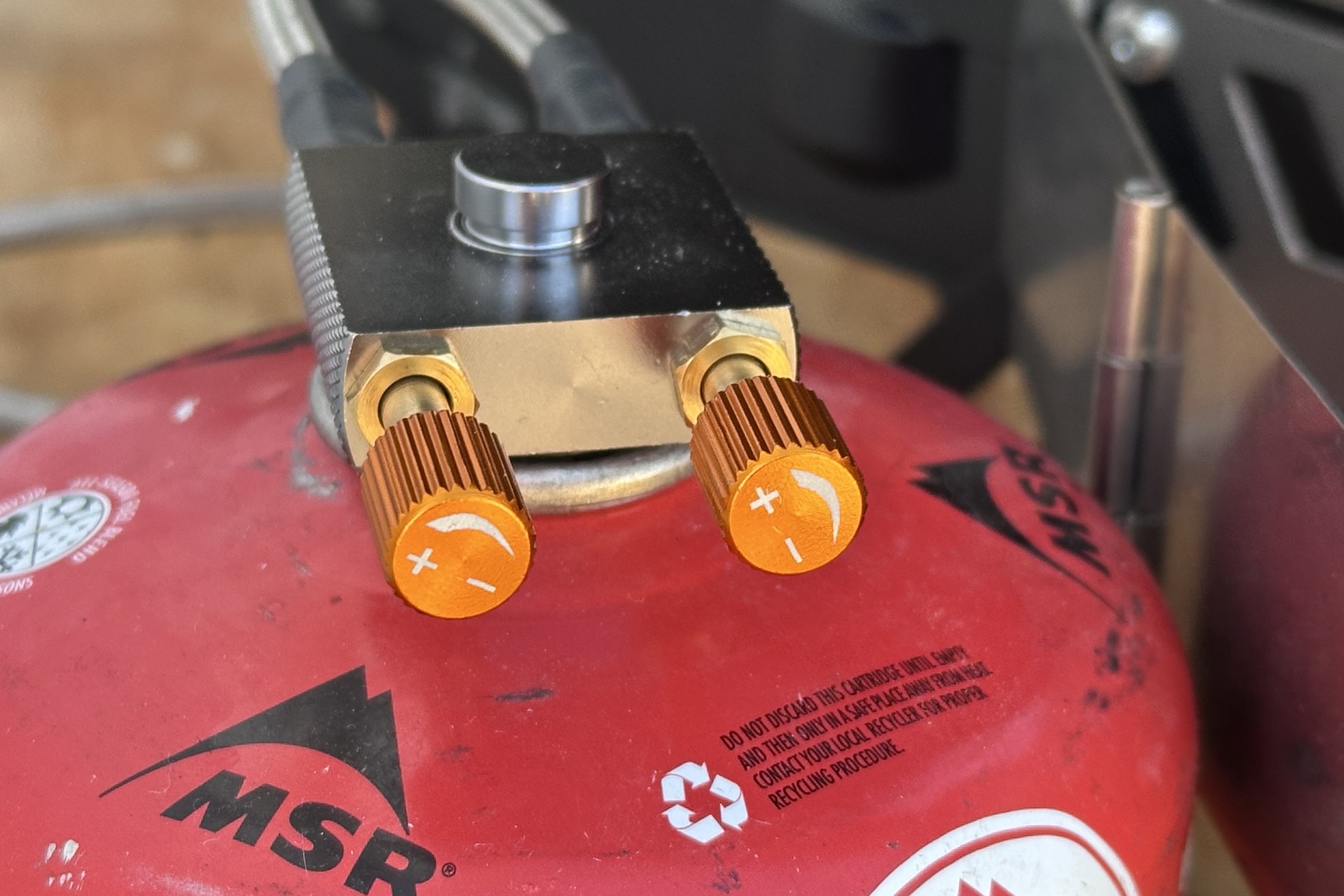 Close-up image of two orange flame-control dials on a fuel line attached directly to a red fuel bottle.