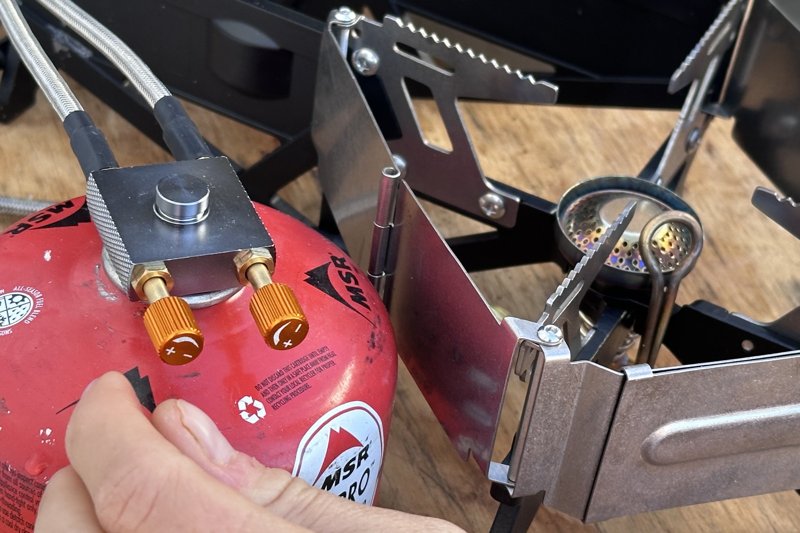 Close-up image of two orange flame-control dials on a fuel line attached to a red butane fuel bottle.