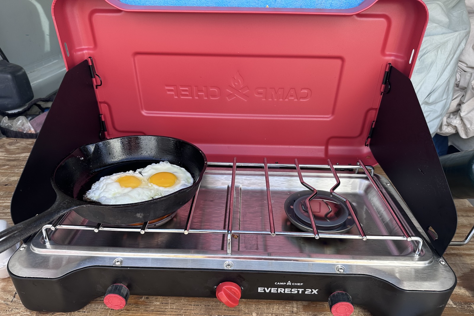 Close-up image of a large double-burner stove with a red hood. Two fried eggs are cooking in a small cast iron skillet on one of the burners.
