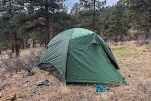 The Kelty Wireless 6 tent pitched at a forest campsite with the rainfly fully deployed and the front vestibule closed.